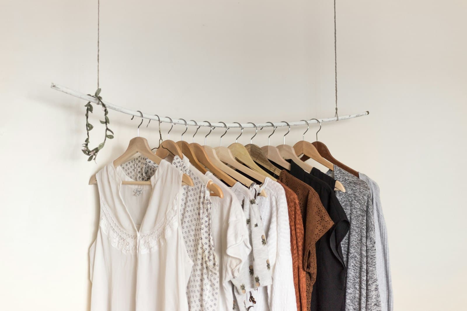 Women's cream, rust, and grey garments hanging on wooden hangers against a warm wall.