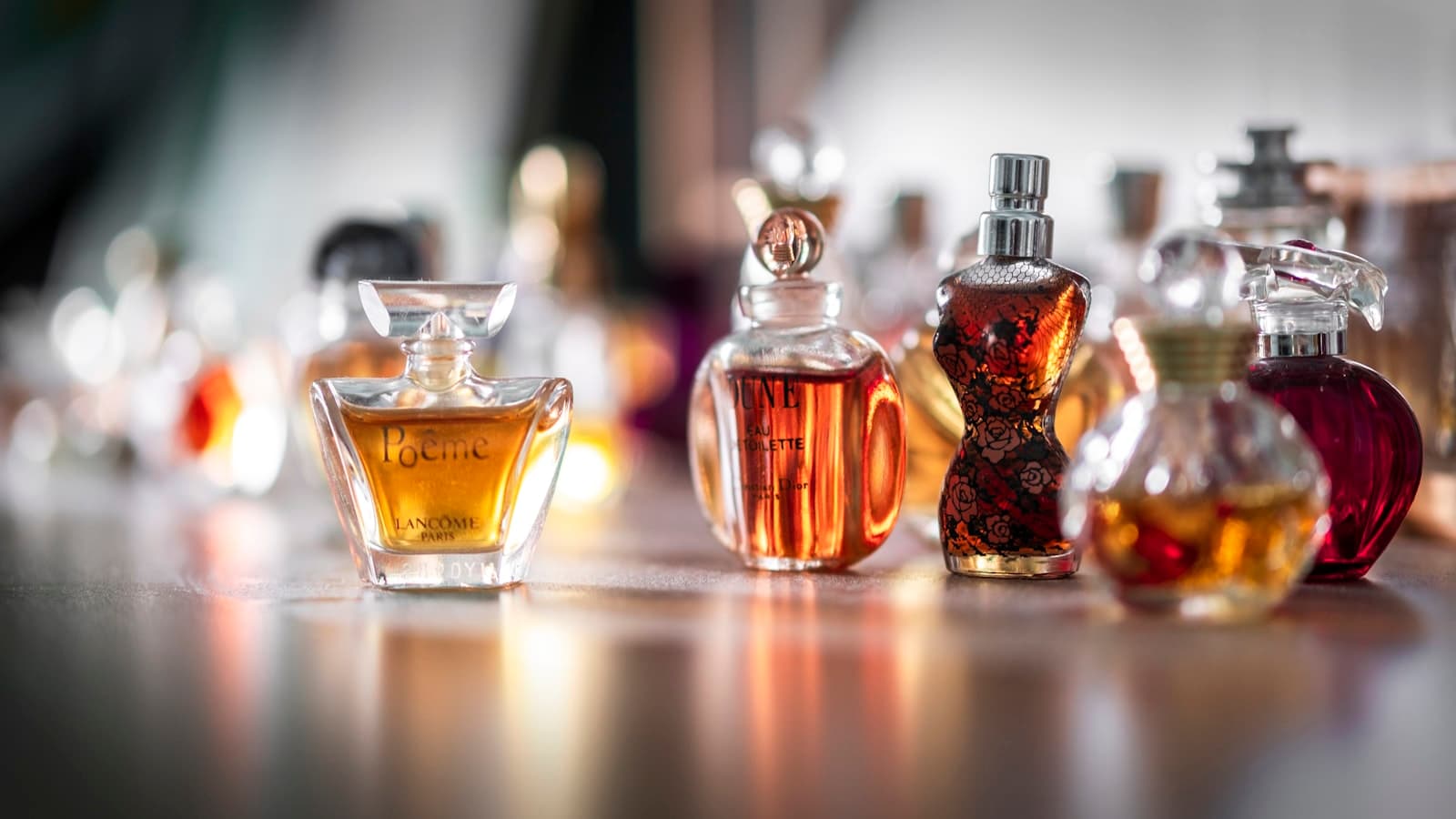 A mixed still of luxury perfume bottles on wood, including Lancôme, Dior, and Jean Paul Gaultier.
