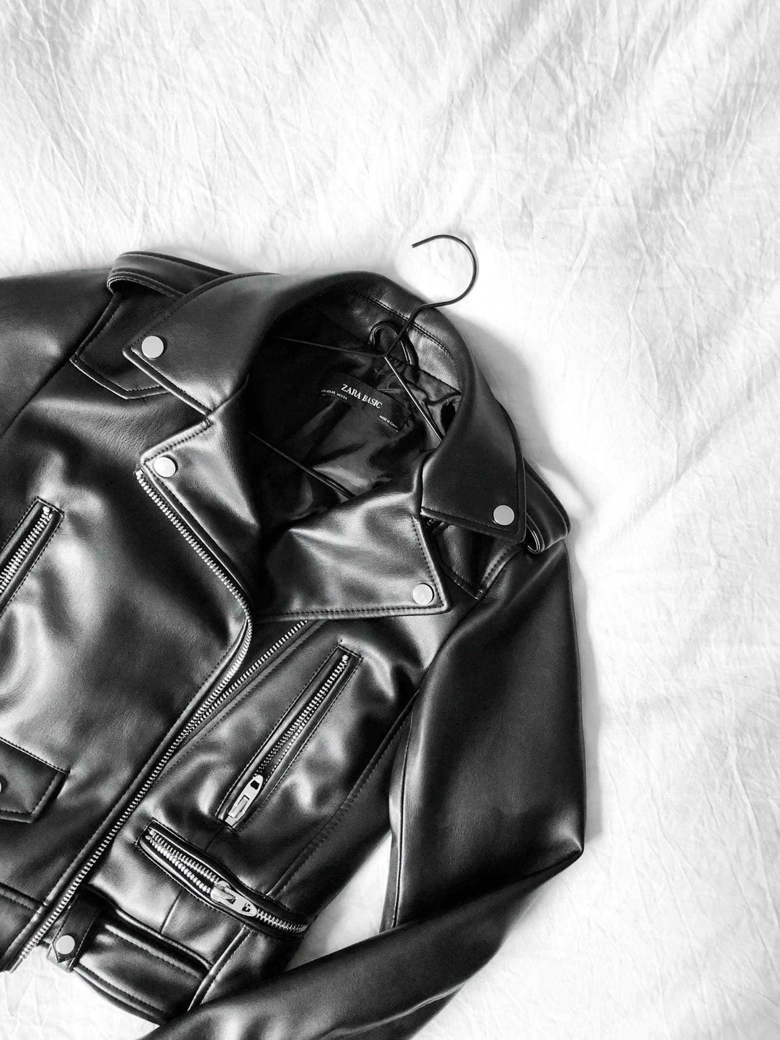 A black leather biker jacket laid on a white sheet, photographed in high-contrast editorial light.