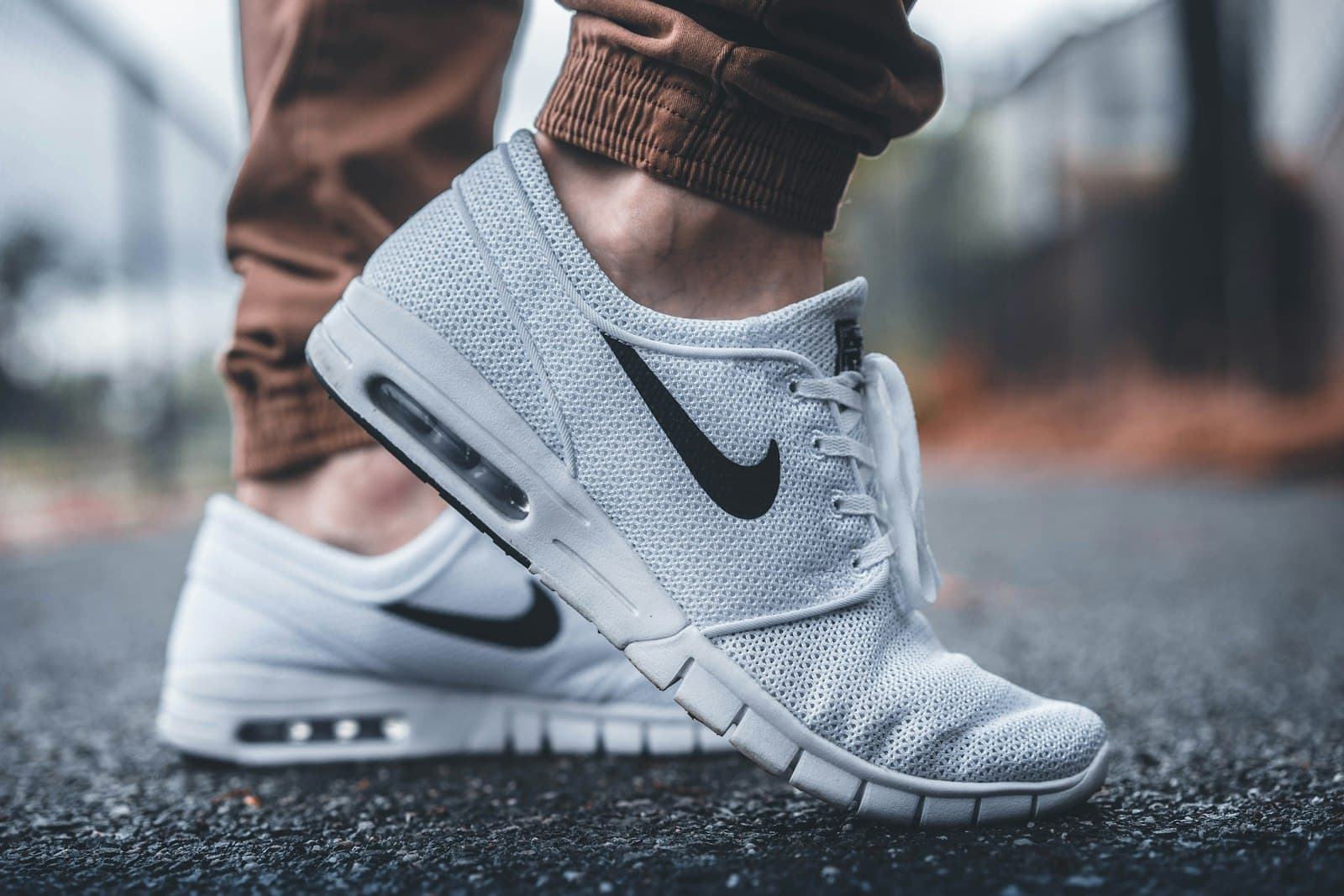 White mesh sneakers worn with tan joggers on an outdoor pavement.